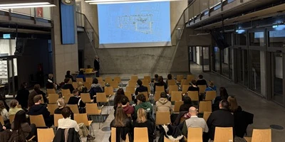 Uczestnicy wykładu Szymona Wojciechowskiego na tle prezentacji projektów APA — miniatura.webp